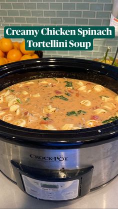 a crock pot filled with creamy chicken spinach tortellini soup next to oranges