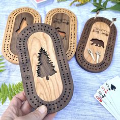 a person holding up some wooden magnets with animals and trees on them next to playing cards