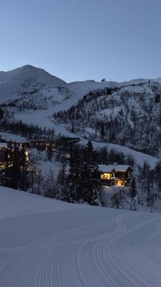 a snow covered ski slope with houses on the side and mountains in the background at night