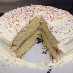 a cake with white frosting and sprinkles is cut in half on a plate