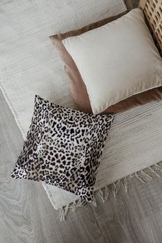 two pillows and a pillow on a bed next to a wicker chair with an animal print cushion