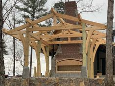 an outdoor fireplace built into the side of a building with wood framing around it and surrounded by trees