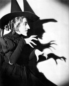 a black and white photo of a woman in a witch costume with her hands out