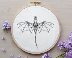 a cross stitch pattern with a bat on it and purple flowers in the foreground