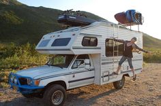 a man standing on the back of a truck with a camper attached to it