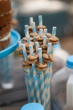 there are many cookies and cupcakes in the glass on the table with blue striped paper straws