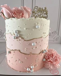 there is a pink and white cake with flowers on the top, and a gold happy birthday sign in the middle