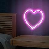 a heart shaped neon sign sitting on top of a wooden table next to a bed