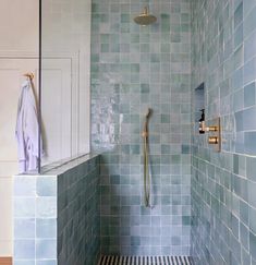 a bathroom with blue tiles and a shower head in the corner, next to a white cabinet