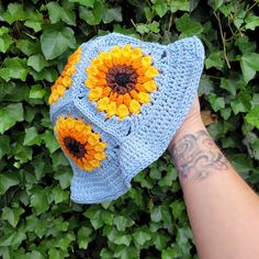 a hand is holding up a crocheted hat with sunflowers on it