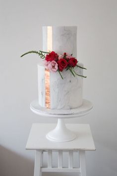 a white marble cake with red flowers on top sitting on a small table in front of a white wall