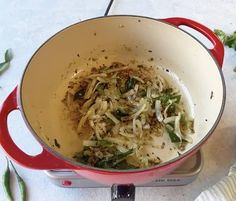 a red pot filled with food sitting on top of a counter next to green peppers