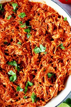 mexican shredded meat in a skillet with cilantro and limes on the side