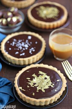 chocolate tarts with gold flecks on black plates next to a fork and glass of orange juice