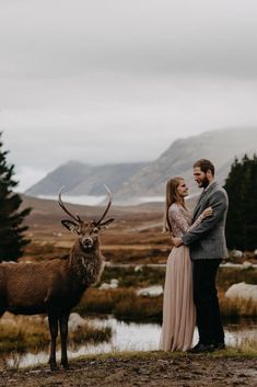 a man and woman standing next to each other near a deer