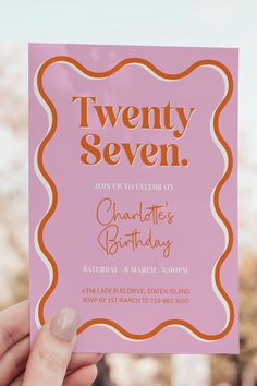 a person holding up a pink card with the words twenty seven in orange on it