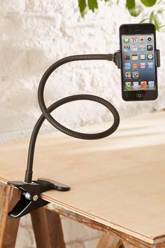 an iphone is hooked up to a phone holder on a wooden table with a plant in the background