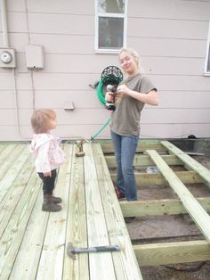 a woman is holding a hose and standing next to a toddler on a wooden deck