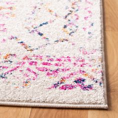 a white rug with multicolored floral designs on the top and bottom corner is laying on a wooden floor