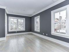 an empty room with two windows and hard wood flooring on the far wall is painted gray