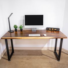 a wooden desk with a computer monitor and keyboard on it, in front of a white wall