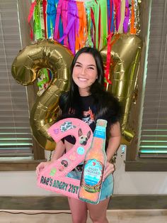 a woman holding up a bottle of booze in front of balloons