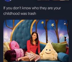 a woman sitting on top of a blue couch next to a stuffed animal and smiling