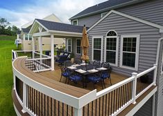 a deck with chairs and an umbrella on it in front of a gray house surrounded by green grass