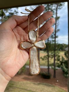 a person holding up a cross made out of seashells in front of a window