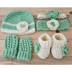 a crocheted hat, booties and mittens are laid out on a wooden surface