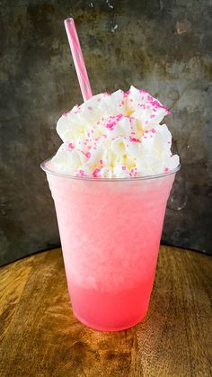 a pink drink with whipped cream and sprinkles in a plastic cup on a wooden table