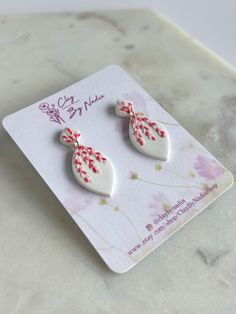 pair of white and red earrings with flowers on them sitting on top of a card