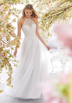 a woman in a white dress standing under a tree with pink flowers on the branches