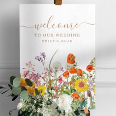 a welcome sign with colorful flowers and greenery in front of a white background that reads, welcome to our wedding