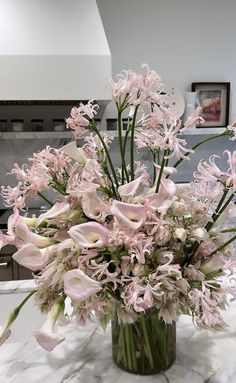 a vase filled with lots of pink flowers on top of a marble countertop in a kitchen