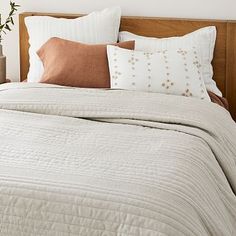 a bed with pillows and blankets on top of it next to a vase filled with flowers