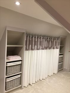 an empty room with white curtains and baskets on the shelf next to it, along with other items