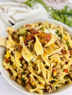 a white bowl filled with pasta, meat and veggies on top of a table