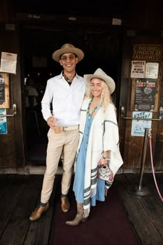 a man and woman are standing on a wooden deck together wearing cowboy hats, scarves and boots