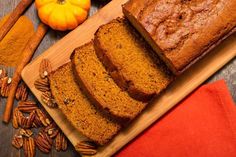 slices of pumpkin bread on a cutting board with pecans and cinnamons around it