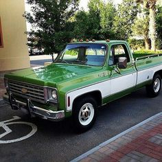 a green and white pickup truck parked on the side of the road in front of a building