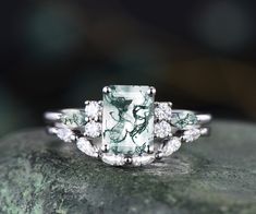 a green and white stone ring sitting on top of a mossy rock with diamonds around it