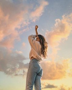 a woman standing on top of a hill with her arms in the air and looking up