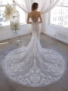 the back of a woman in a wedding dress standing near a birdcage with flowers on it