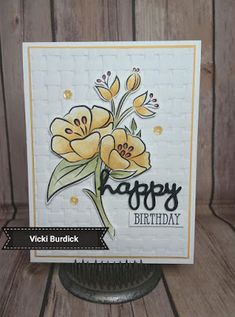 a happy birthday card with yellow flowers on the front and bottom, sitting on a wooden surface