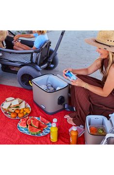 a woman sitting on the ground next to an open cooler with food in front of her