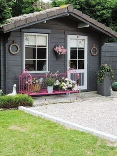 a small gray shed with flowers and potted plants