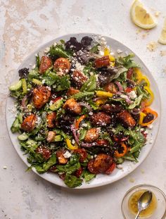 a white plate topped with a salad next to a glass of wine and lemon wedges