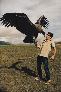 a man holding an eagle in his hand while standing on top of a grass covered field