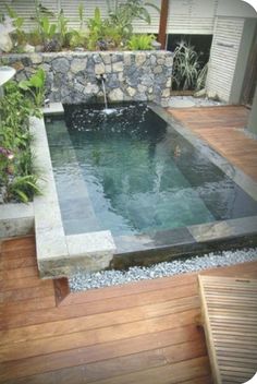 an outdoor swimming pool surrounded by wooden decking and stone walls, with a waterfall in the middle